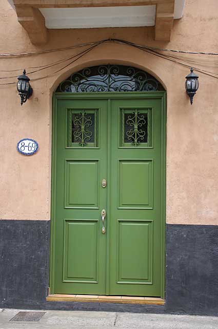 Photo Example of a traditional old door in green color with small top windows covered with a metal decor, the image of this door was taken in "El Casco Viejo", the old colonial part of Panama City.