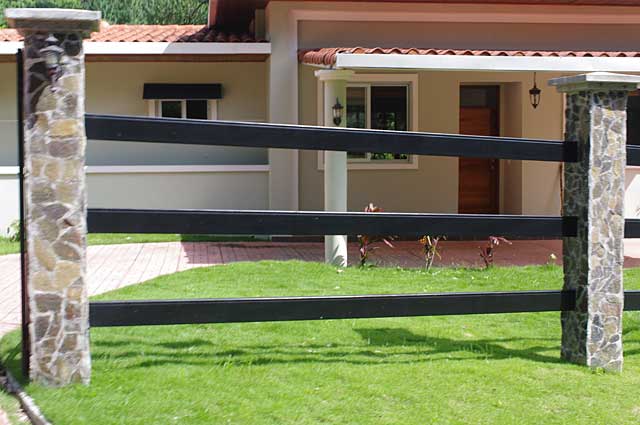 Photo Example of a elegant country style fence with natural stone columns and black metal bars. 