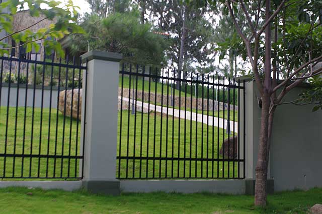 Photo Example of a fence made of grey and olive green cement columns and black metal bars