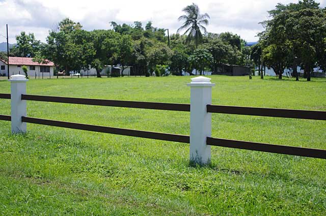 Photo Example of a simple fence around a country home with white columns and dark brown bars