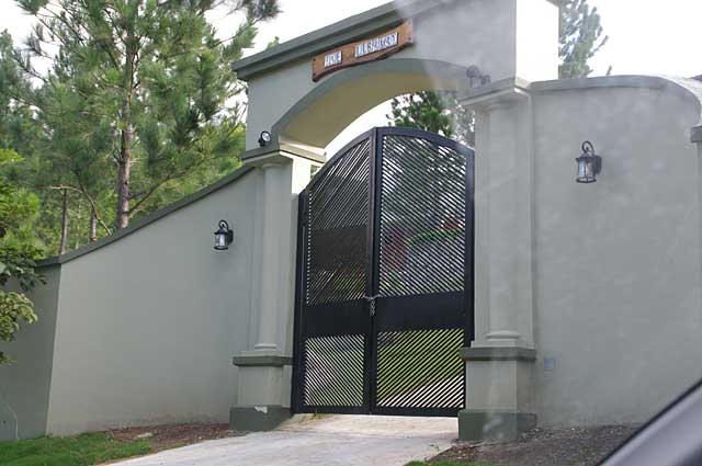 Photo example of a luxurious black metal gate surrounded by olive green columns and walls