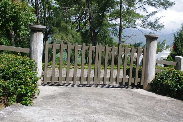Photo of a simple gate made of raw cement stone pillars and olive green gates