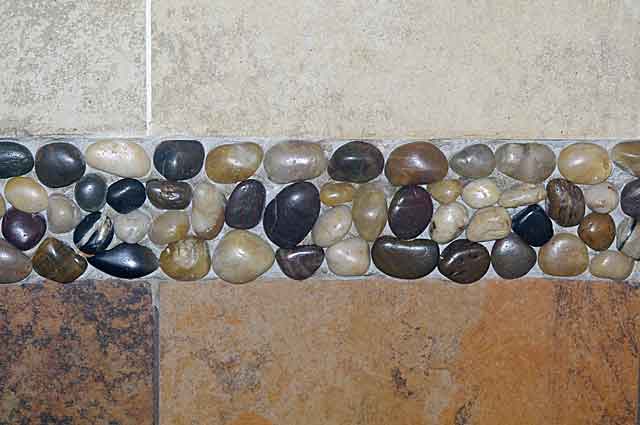 Photo example of a bathroom wall with small river stones (marbles sized) forming a decorative division between 2 different colored tiles