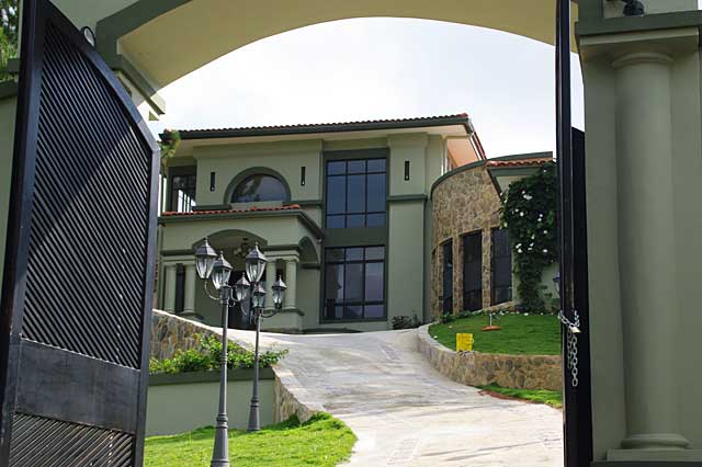 Photo of a big light olive green painted townhouse with black window frames. Note the natural stone walls that are very decorative